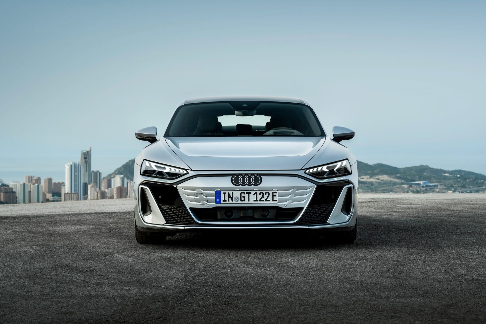 Frontal vy av en silverfärgad Audi e-tron GT med en stad i bakgrunden