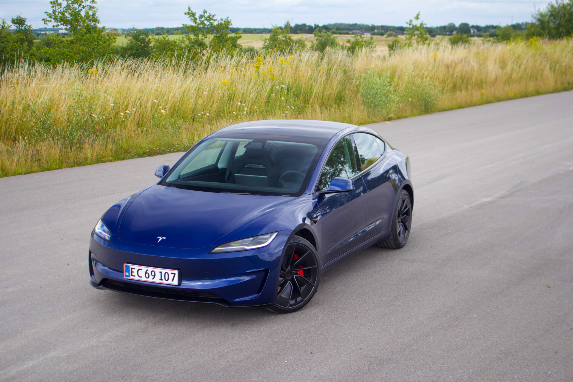 En mörkblå Tesla Model 3 fotograferad snett framifrån, stående på en landsväg.