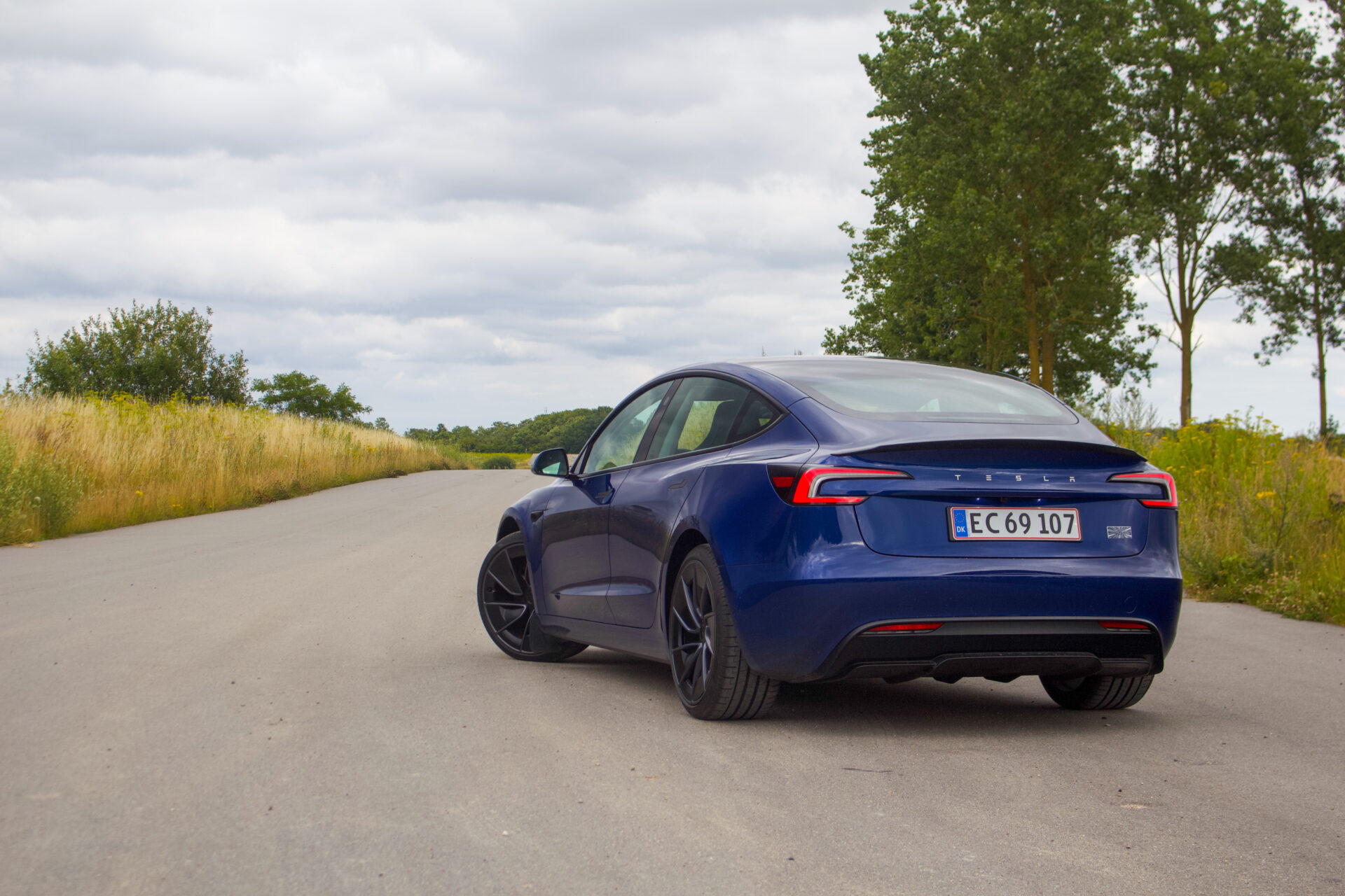 En mörkblå Tesla Model 3 fotograferad snett bakifrån på en landsväg.