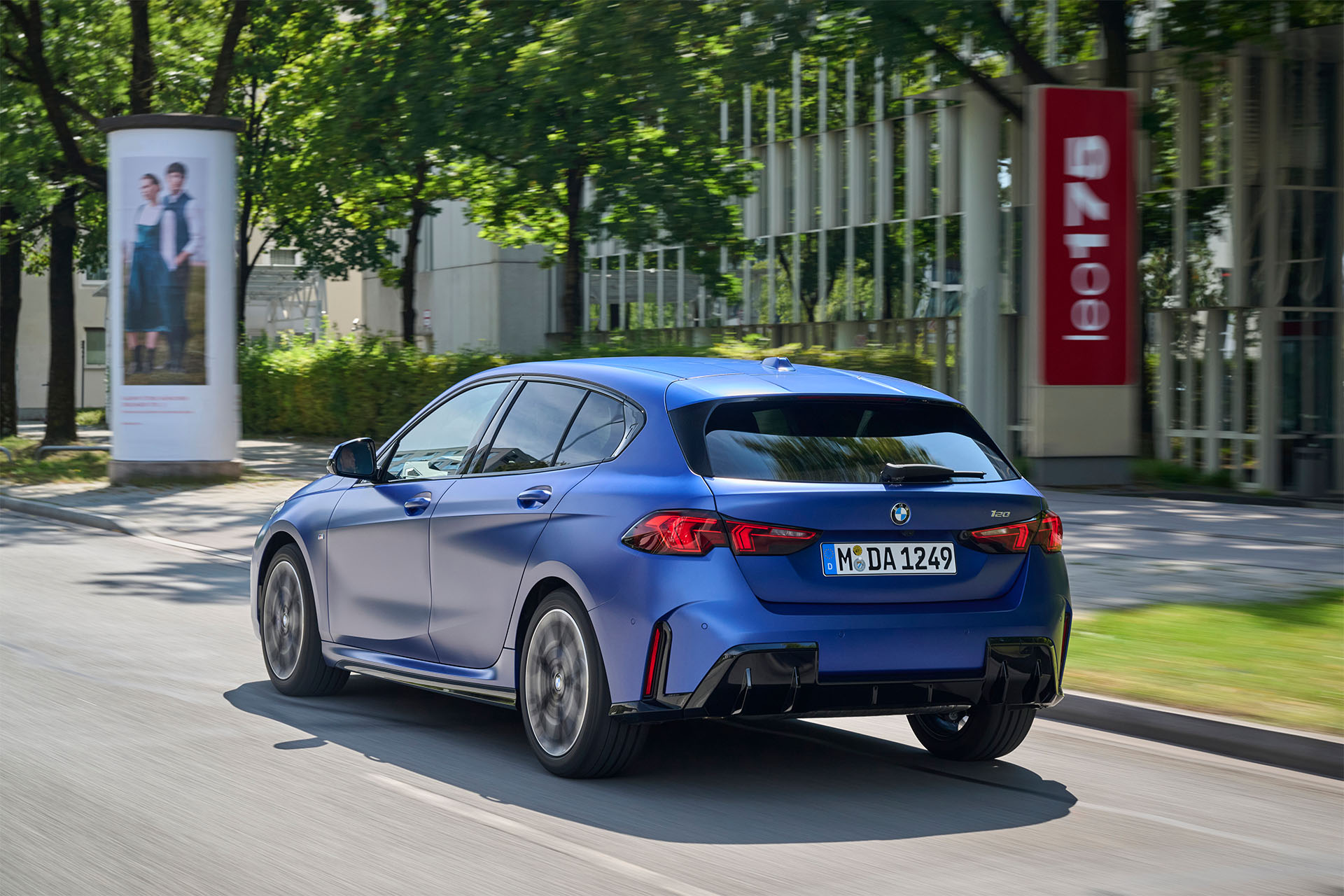 Blå BMW 120i som kör på en stadsväg omgiven av grönska.