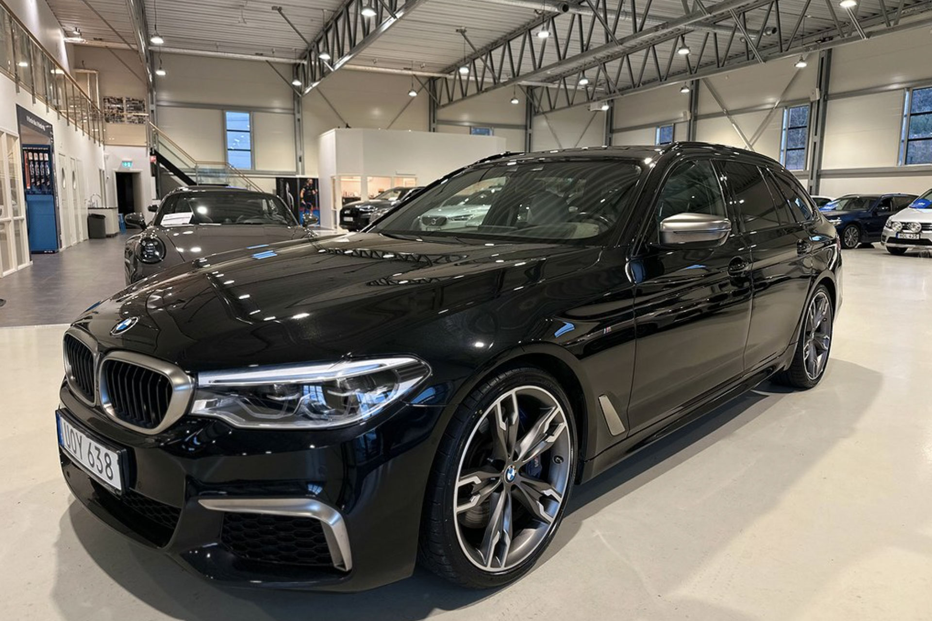 En svart BMW parkerad i en bilhall, sett framifrån i ett upplyst showroom.